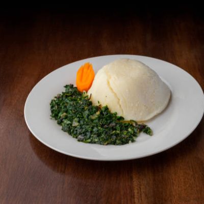 Ugali / Cornmeal Mush and vegetable dish served on a white plate on a wooden table. African