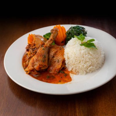 Chicken stew and rice dish served on a white place on a wooden table. Delicia African chicken stew with rice